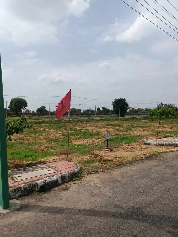 Vacant kerbed plots inside Lifestyle City with a plot-number marker and a developer flag, houses on the horizon, Alwar Bypass Road, Bhiwadi