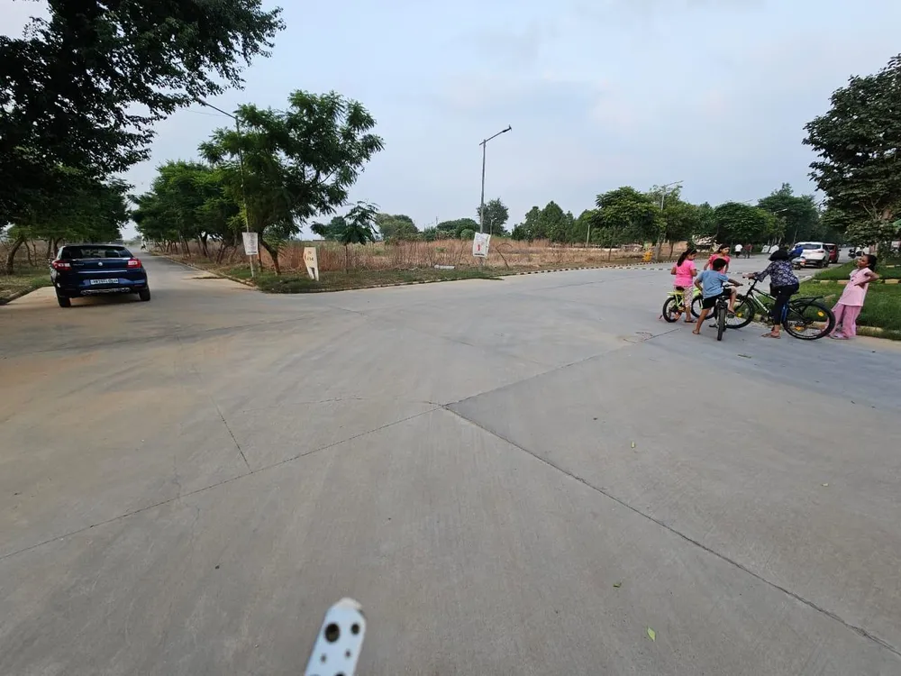 Wide concrete road crossing in the Terra City plotted sector, with vacant plot land and a plot marker board beyond, Alwar Bhiwadi Road, Bhiwadi