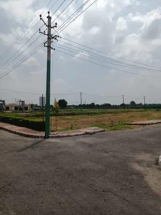 Sector road and vacant plots inside Lifestyle City, with completed houses to one side and street power poles along the boundary