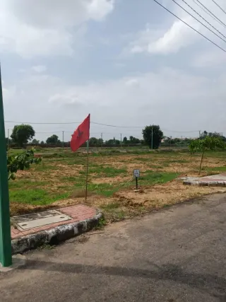 Vacant kerbed plots inside Lifestyle City with a plot-number marker and a developer flag, houses on the horizon, Alwar Bypass Road, Bhiwadi