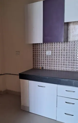 Kitchen fitted with modular units over a granite counter and a mosaic tile splashback, this 3 BHK flat at MVL Coral, Bhiwadi