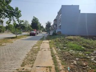 Vacant plot beside a built house on a paved internal road in Omaxe Green Meadow City, Bhiwadi