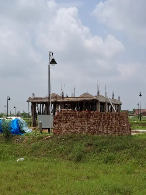A house under construction at Aqasia Enclave, freshly cast roof slab still on timber props with a stack of bricks alongside