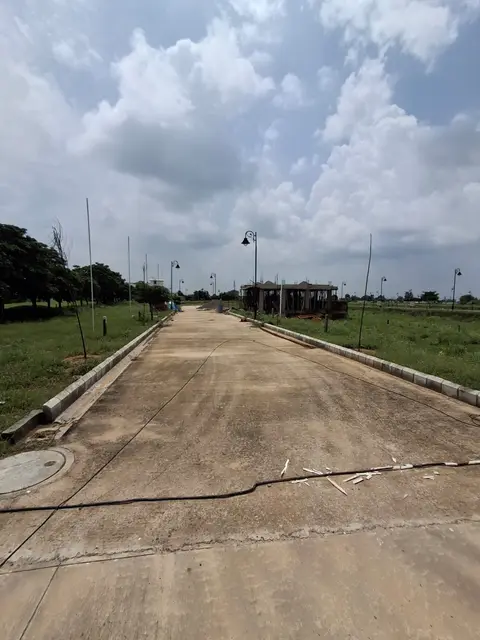 Wide concrete sector road at Aqasia Enclave with cast kerbstones and street lights, a house under construction on a plot alongside