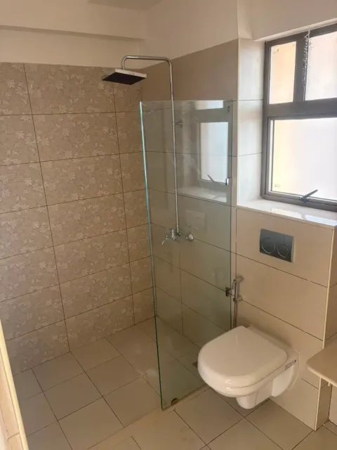 Bathroom with a glass shower partition and wall-hung toilet in an Ashiana Tarang flat, Bhiwadi