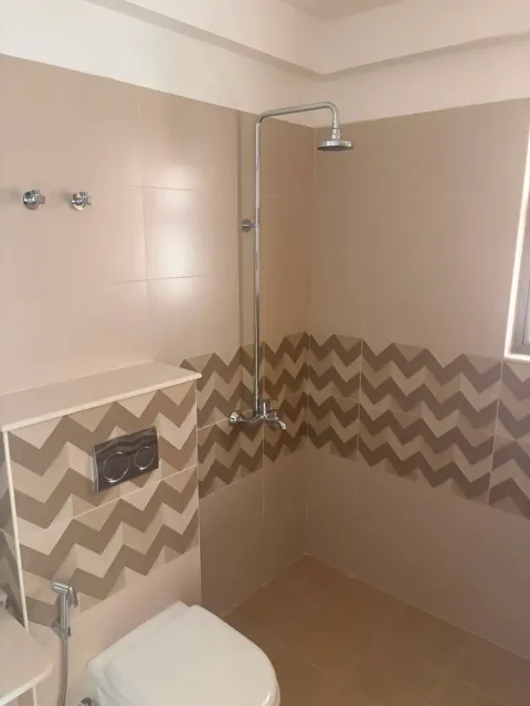 Bathroom with chevron wall tiles and an overhead shower in an Ashiana Tarang flat, Bhiwadi