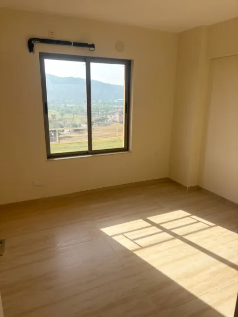 Bedroom with a wide window and wood-finish floor tiles in an Ashiana Tarang flat, Bhiwadi