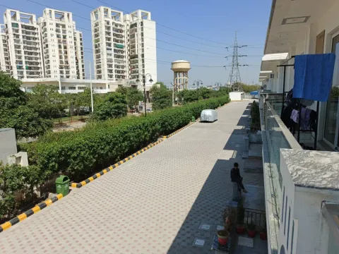 Paved road inside the boundary hedge of Madhuvan Residency with the Ashiana towers beyond, Bhiwadi