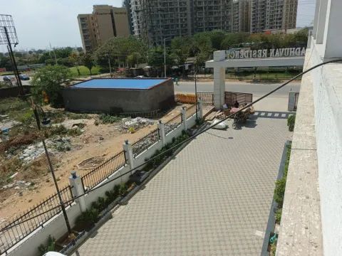Madhuvan Residency entrance gate and paved approach seen from above, with Ashiana Tarang across the road, Bhiwadi