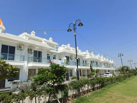 Row of white two-storey villas with balconies behind a lawn and street lamps in Madhuvan Residency, Bhiwadi