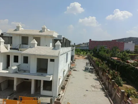 White villas with rooftop kiosks seen from above beside a tree-lined boundary in Madhuvan Residency, Bhiwadi